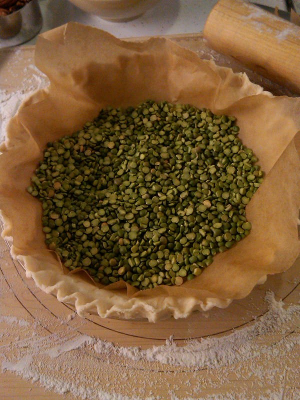 Unbaked pie crust with dried peas on a wooden cutting board.