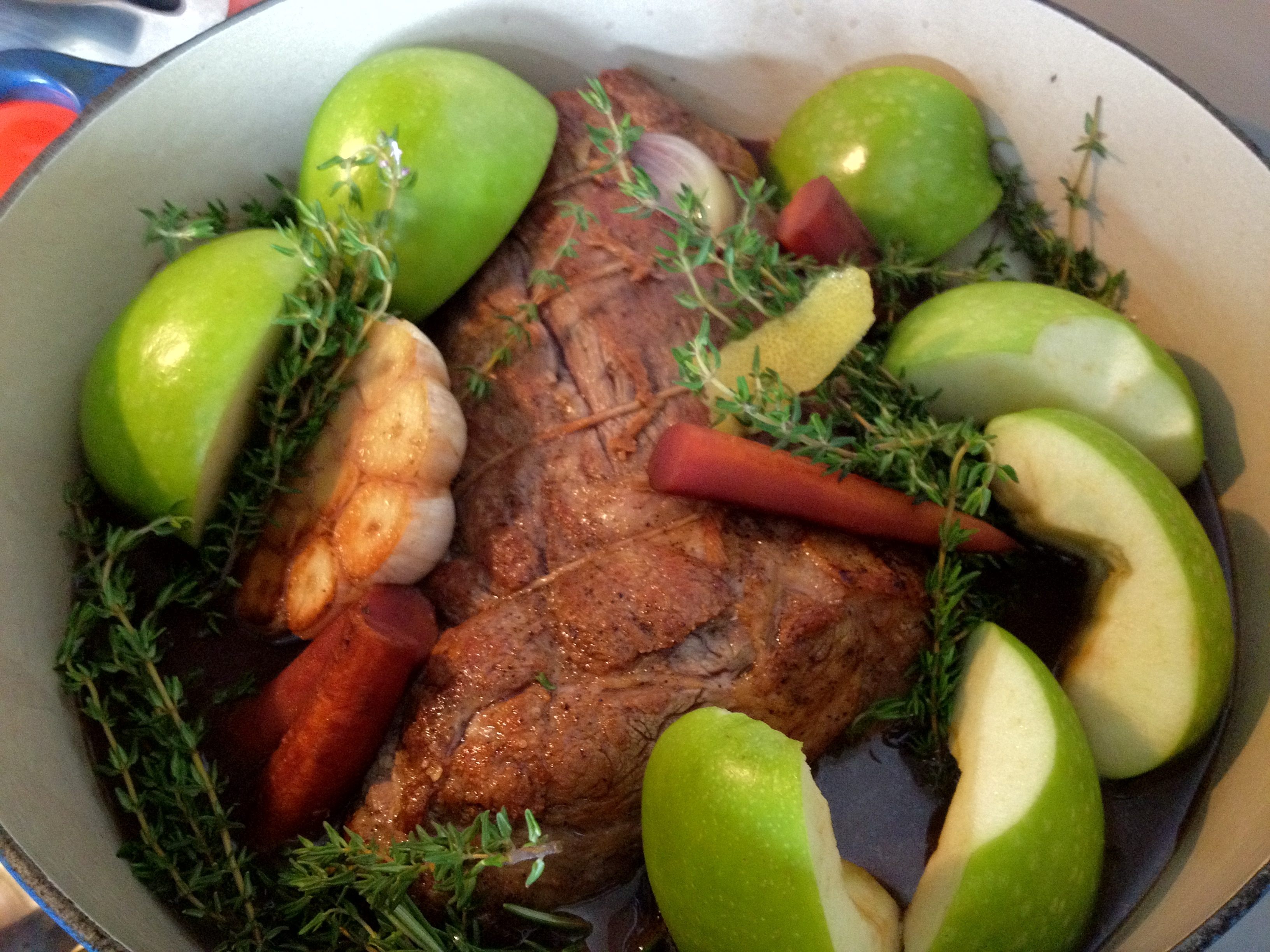 Red wine braised pork roast with apples and thyme in a white dish.