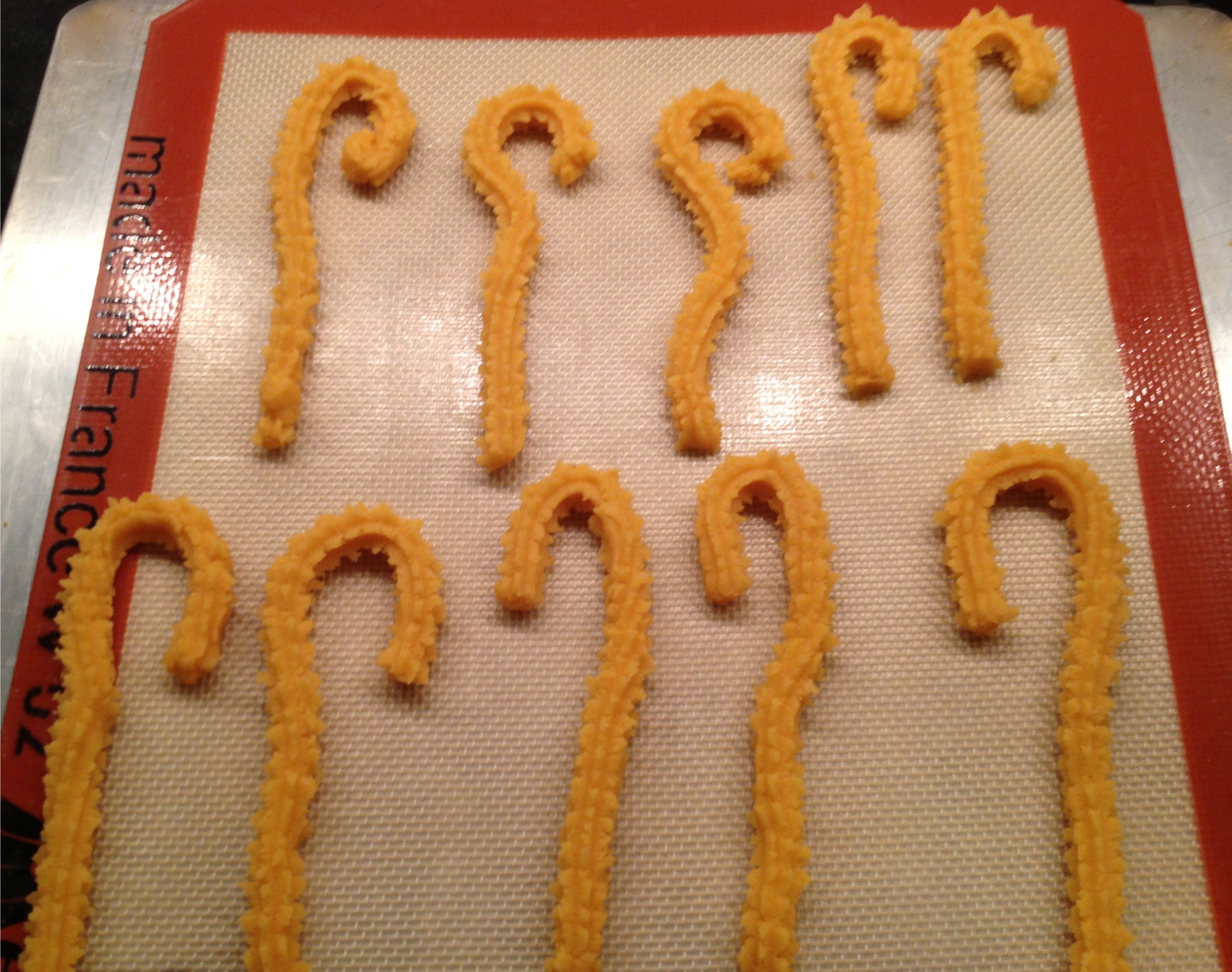 Cheddar cheese straws ready to bake on a siltpad lined cookie sheet.
