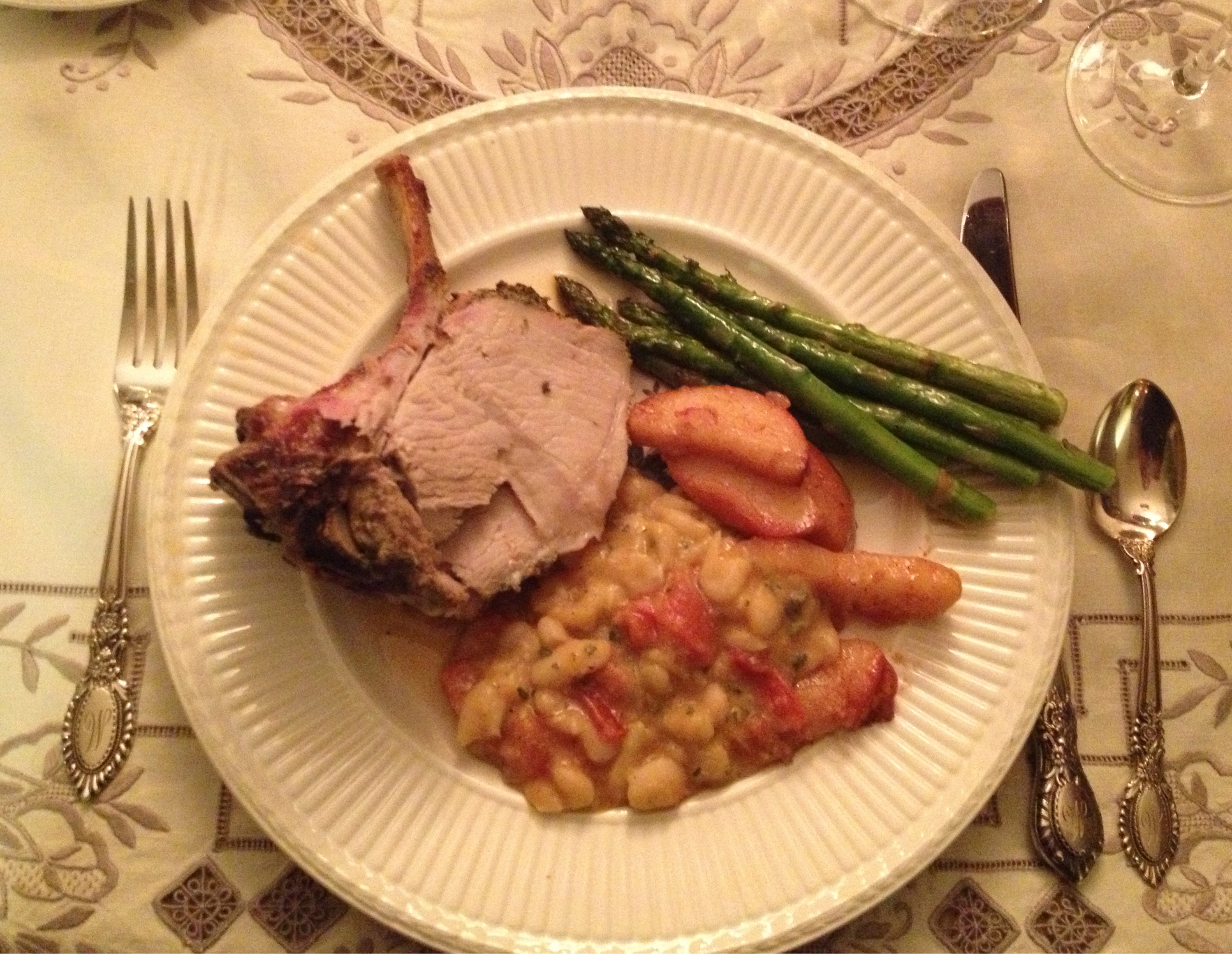 Crown roast of pork with sauteed apples, Italian beans, and roasted asparagus on an antique Wedgewood plate on a beautiful tablecloth