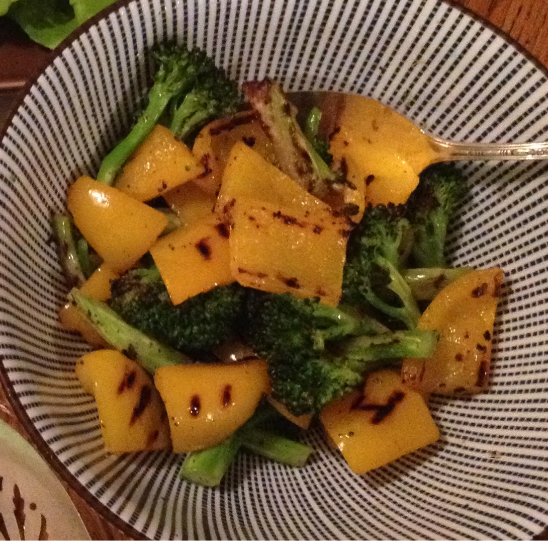 Grilled broccoli and yellow peppers in a blue and white striped bowl..