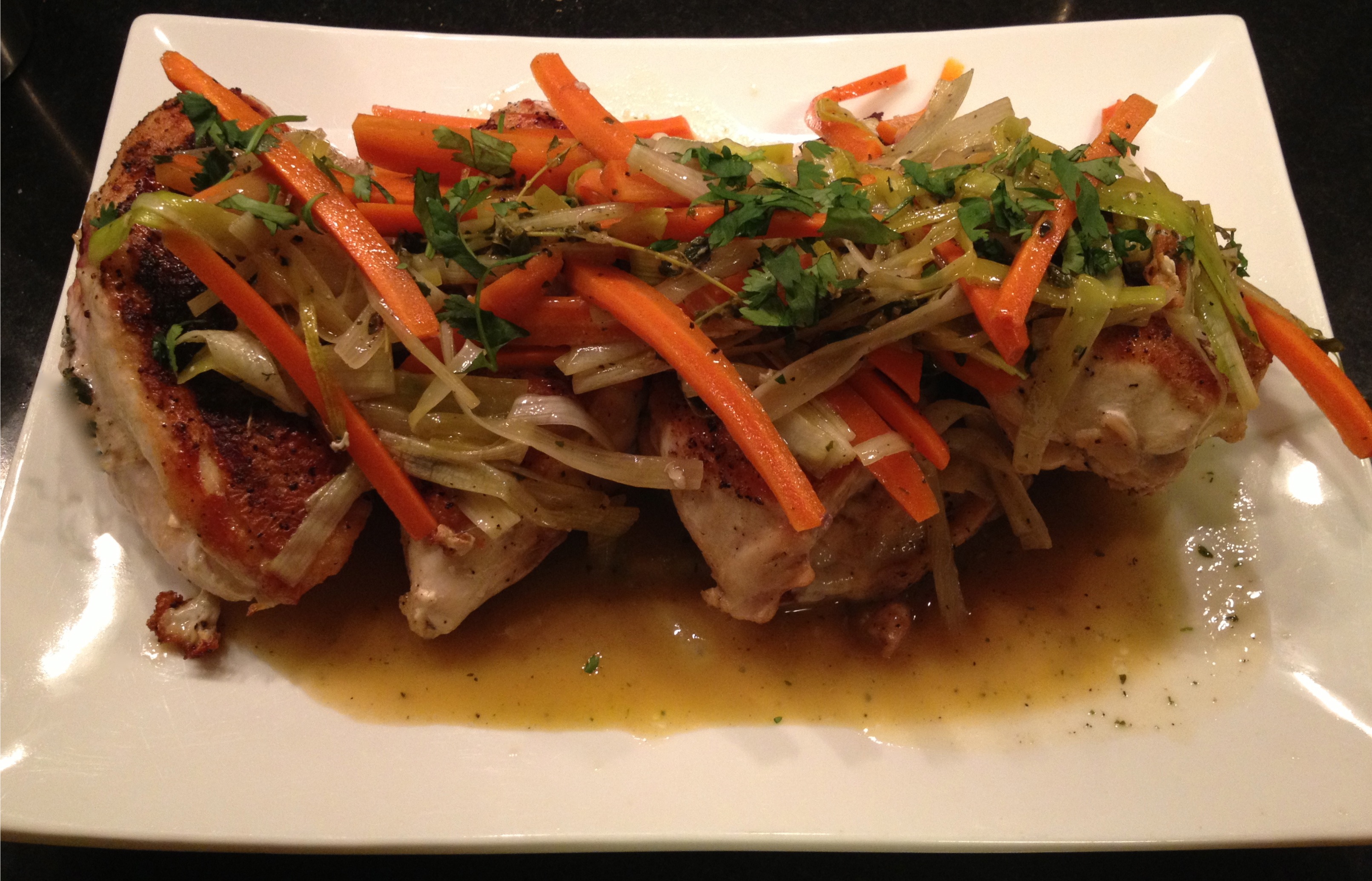 Pan roasted chicken breasts with carrots and leek, garnished with parsley on a white platter.