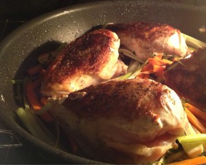 Chicken breasts with carrots and leeks in a skillet, roasting in the oven.