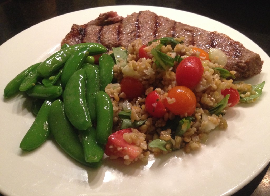 Freekeh salad on a plate with steak and sugar snap peas.