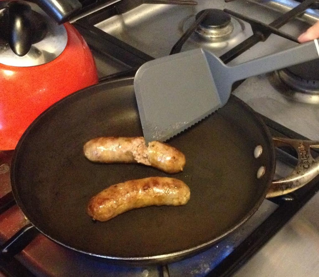 Calphalon serrated spatula cutting pork sausages.