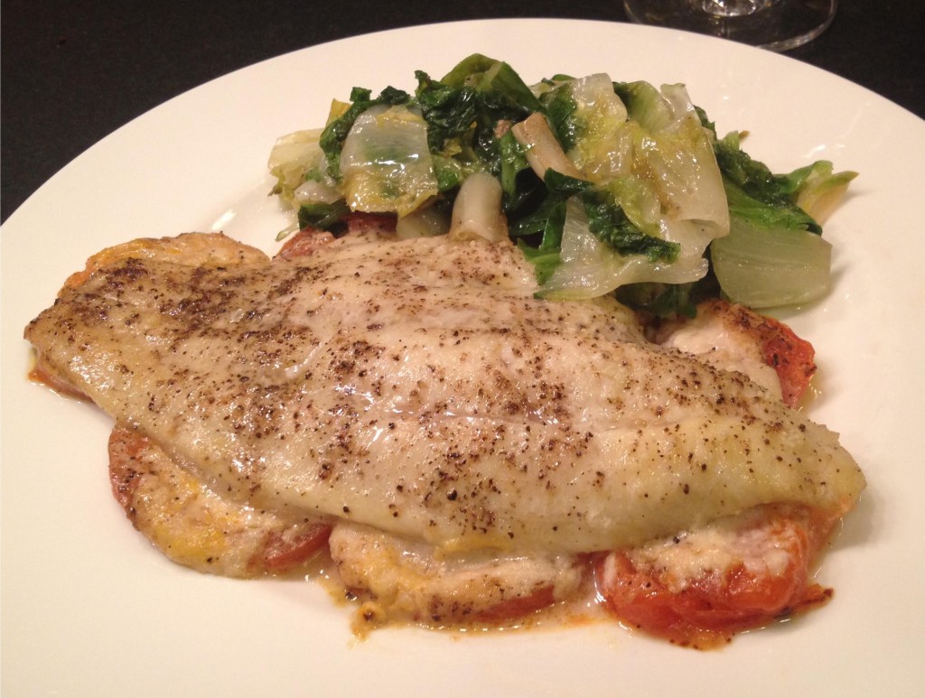 Catfish with tomatoes and horseradish on a plate with sauteed escarole.