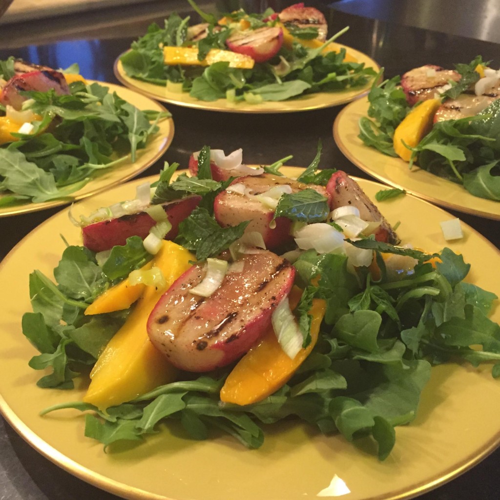 Arugula salad with grilled radishes, mango and mint with a Champagne vinaigrette on a yellow bordered plate.