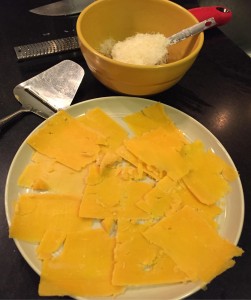 Cheddar cheese slices and Parmigiano grated in a bowl. 