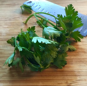 Italian parsley sprigs on a wooden board with a chopping knife.