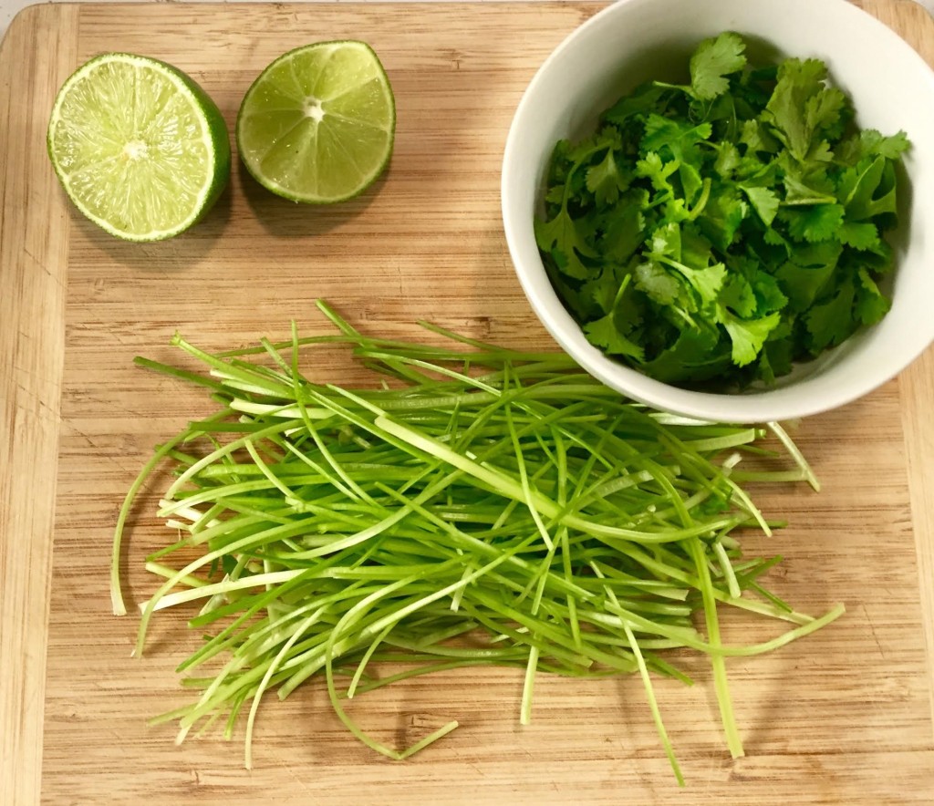 Cilantro stems, leaves and a cut lime on a wooden cutting board.