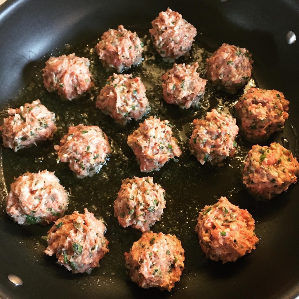 Lamb and veal meatballs with lots of herbs, frying in a skillet.