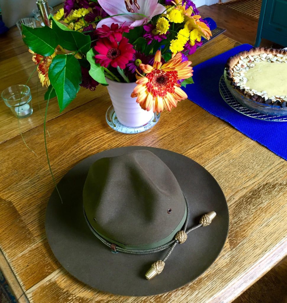 WWII cavalry hat with flowers and pie in the background.