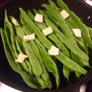 Green flat beans in a skillet with pats of butter on top.