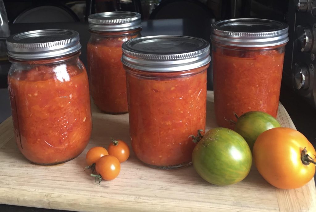 Homemade tomato sauce in glass jars with fresh tomatoes nearby on a cutting board.
