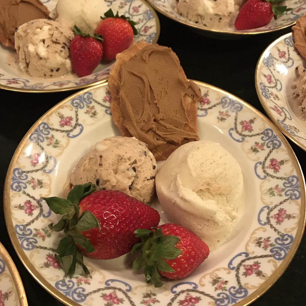 Cookie spread on a butter cookie with two scoops of ice cream and two strawberries in a Limoges bowl.