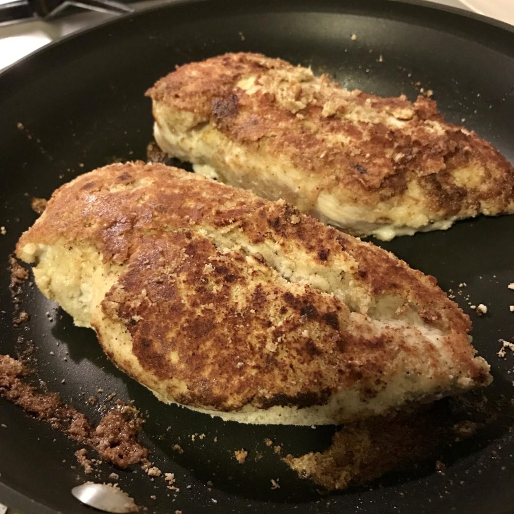 Almond flour on chicken breasts sauteing in a skillet.