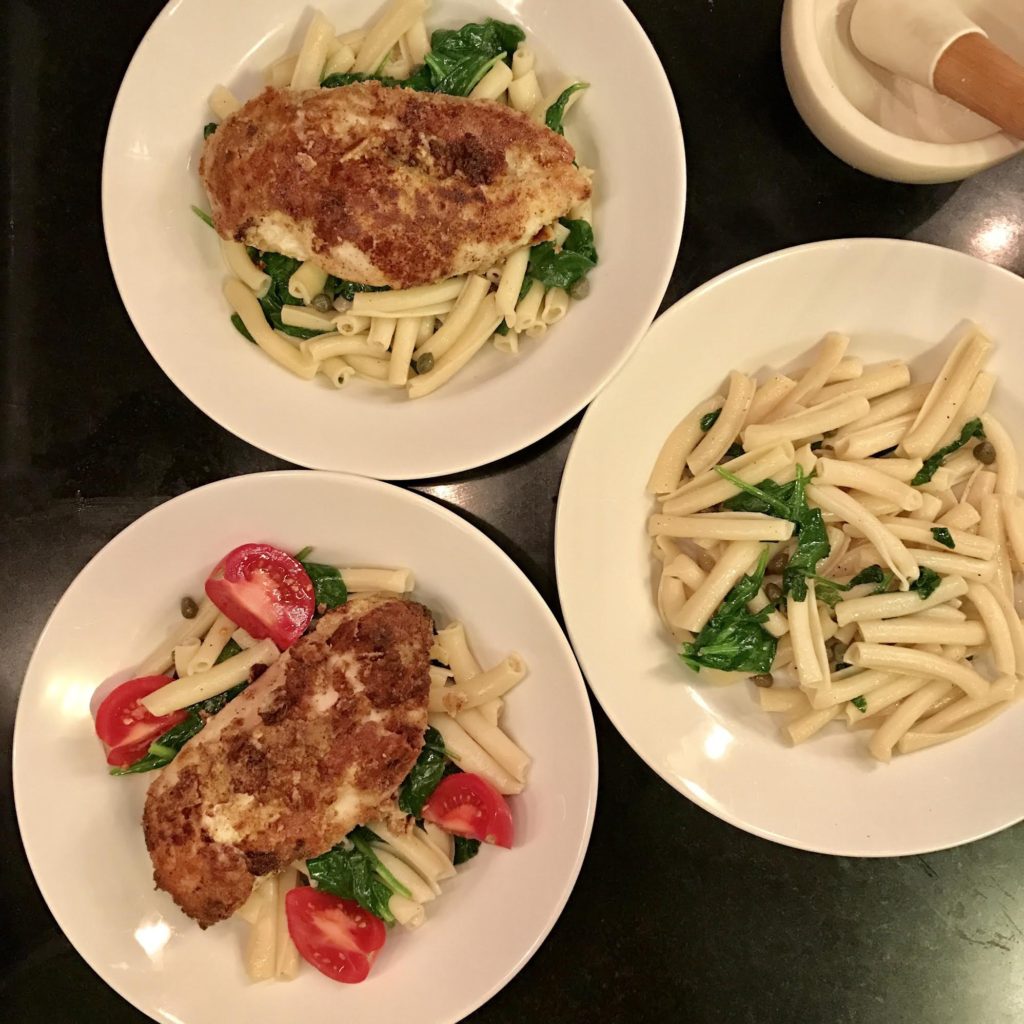 White bowls filled with pasta with baby spinach with almond flour breaded chicken breasts on top.