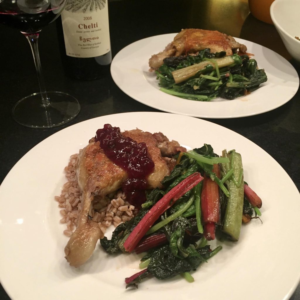 Sauteed duck leg on a white dinner plate with lingdonberries jam and sauteed Swiss chard.