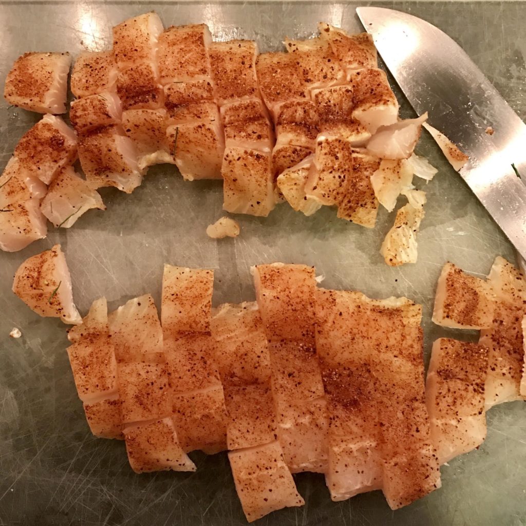 Seasoned fillets of flounder cut into squares on a cutting board.