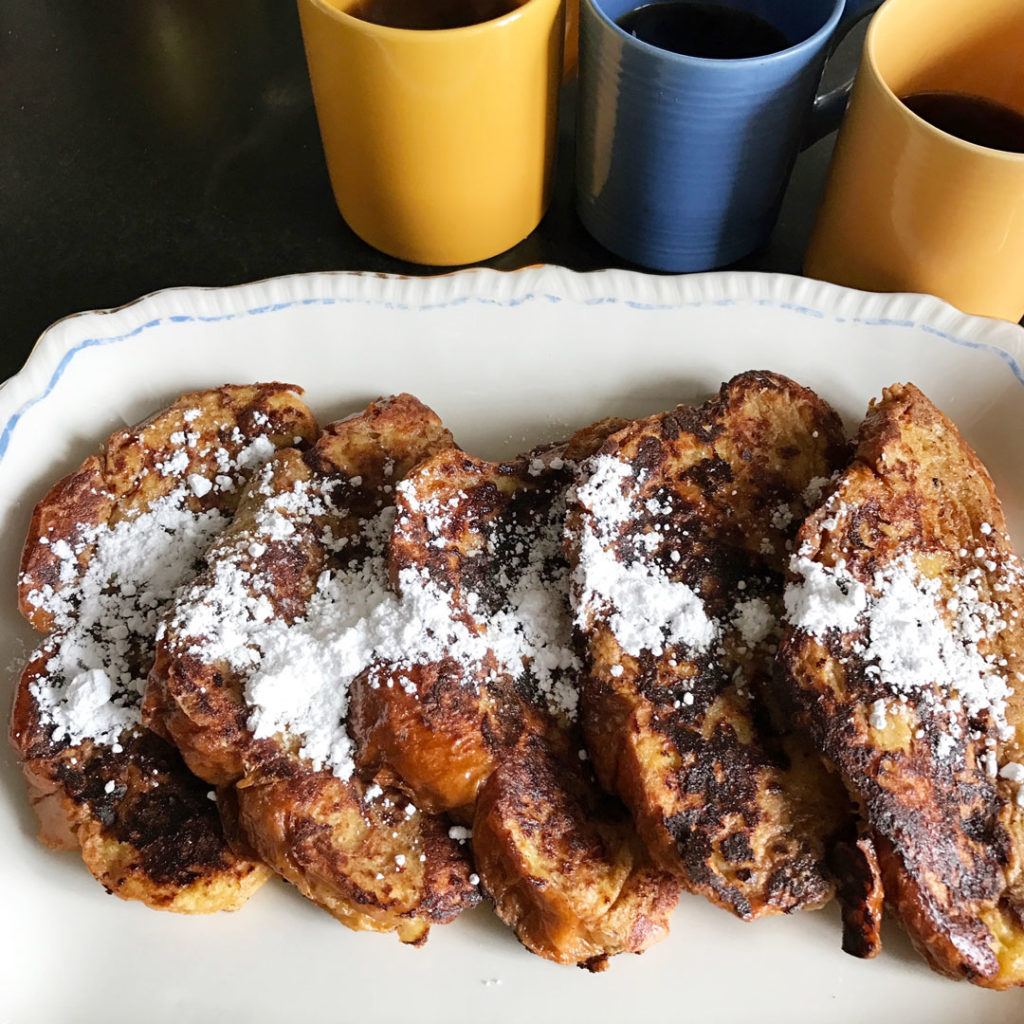 Buttermilk Challah French Toast on an antique white platter with powdered sugar and 3 cups of coffee.