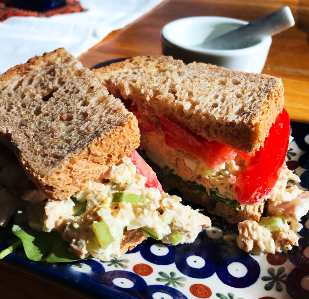 Holy Schmitt's Horseradish tuna salad sandwich cut in half on a blue and white plate.